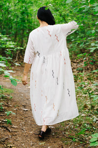 Person wearing an artisan made handwoven white jamdani dress with red and black patterns walking through a forest.