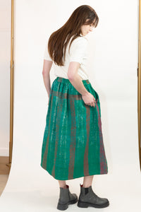 A woman wearing a white short-sleeve top and a vintage kantha quilted Christmas green midi skirt with vertical red stripes, paired with black Chelsea boots, photographed in a studio setting. 