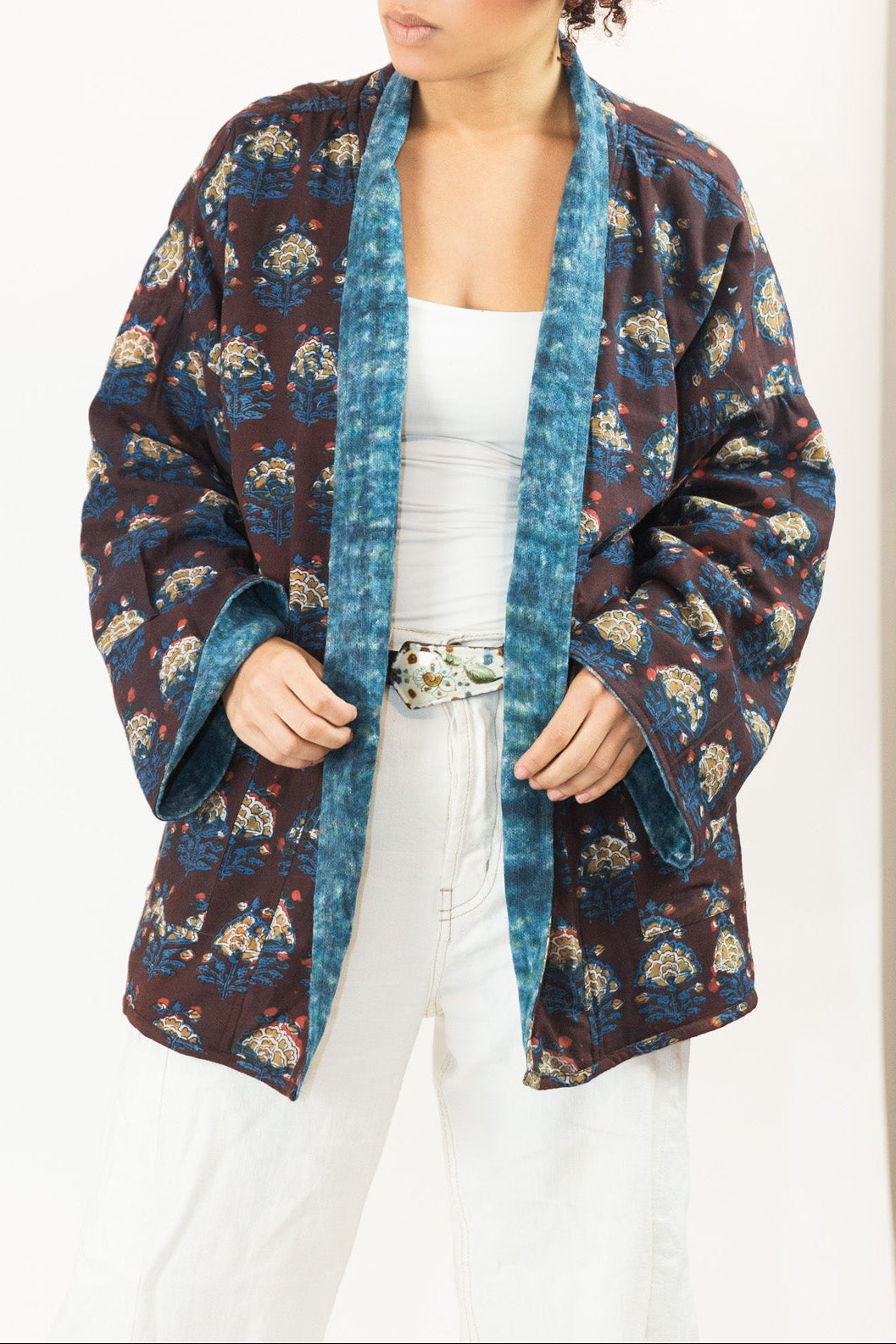 A woman modeling a loose, open-front kimono-style jacket with a dark blue and brown block print , worn over a white top and white pants.