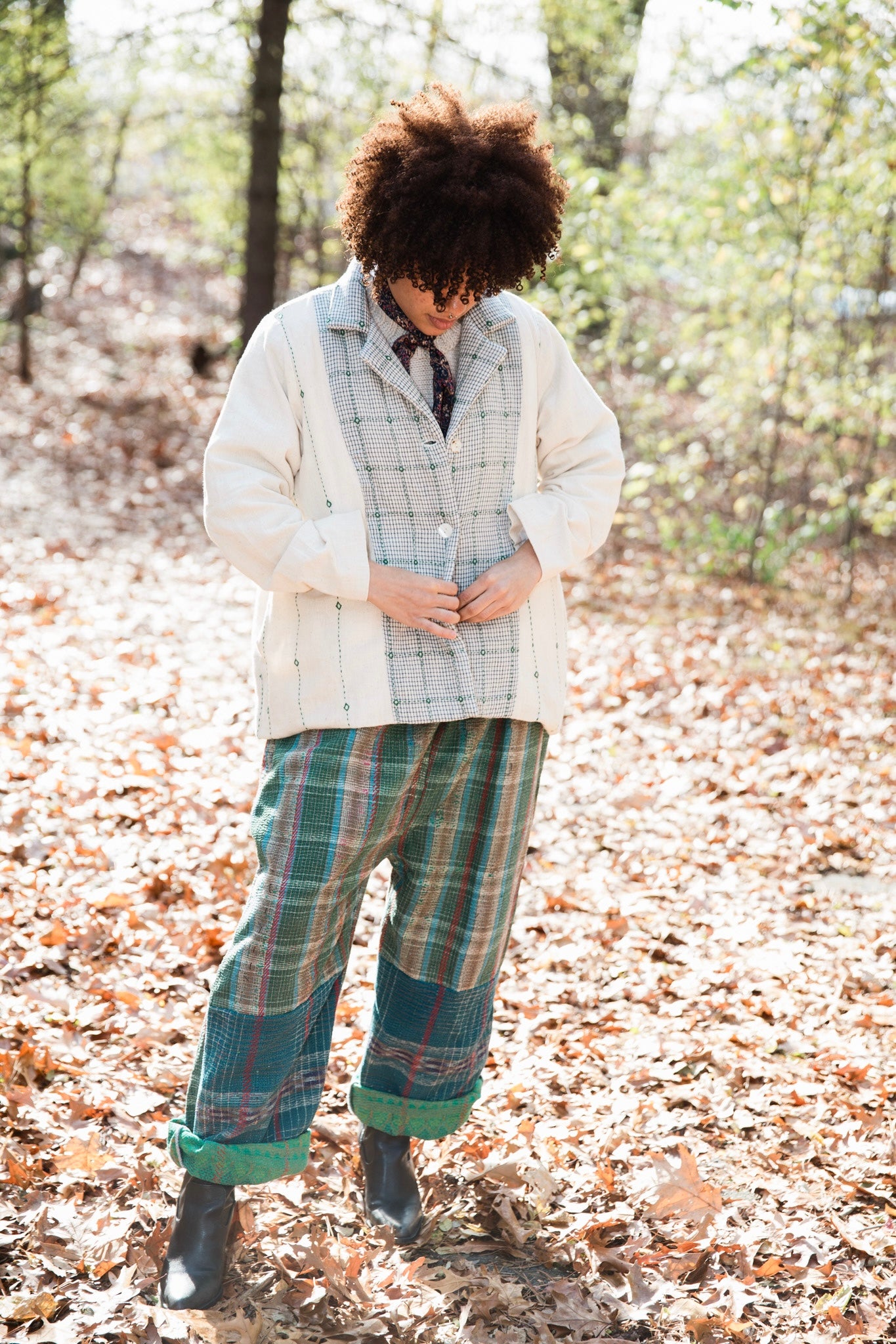 A personal wearing white handwoven artisanal jacket and textured plaid pants  in a forest setting.